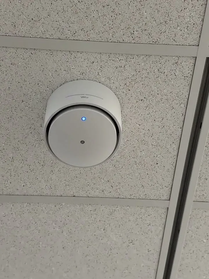 A white ceiling access point with a blue status light