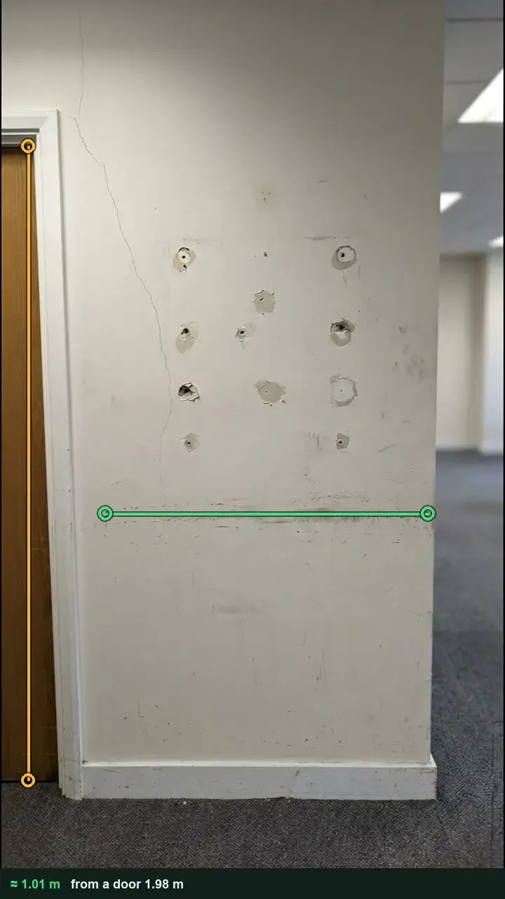 Office wall with screw holes from removed shelving and a scuffed band, measured against the door beside it