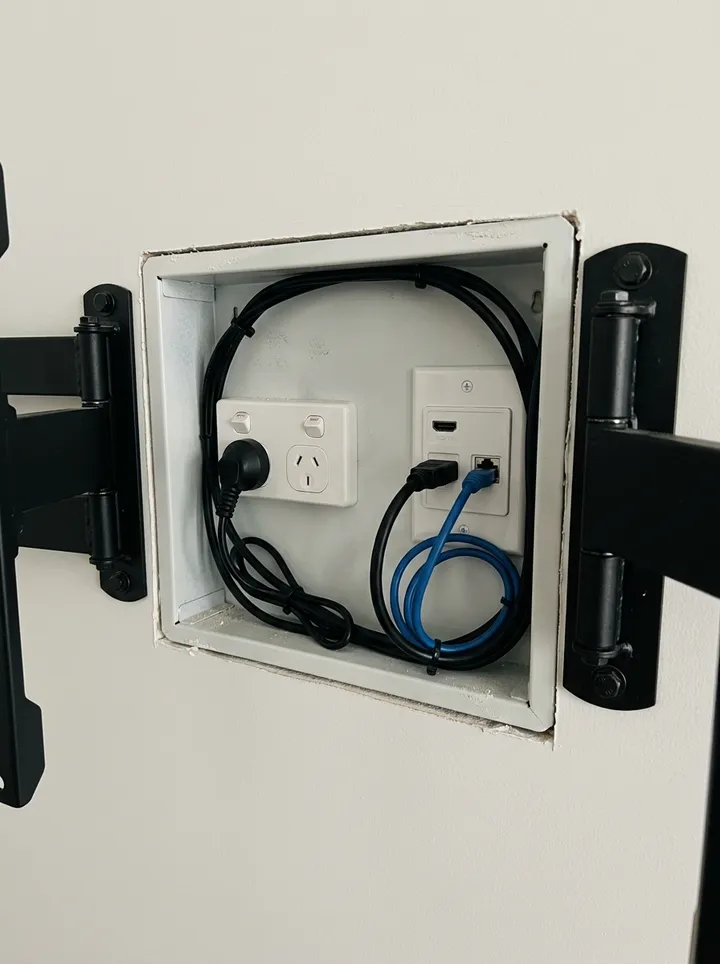 A recessed back box with power and a data wall plate between the arms of a screen bracket