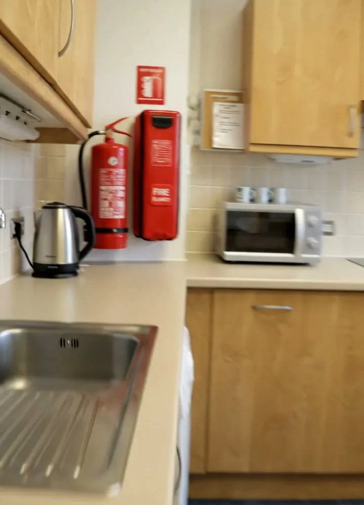 A water fire extinguisher and a fire blanket on the wall of an office kitchenette, beside a kettle and a microwave