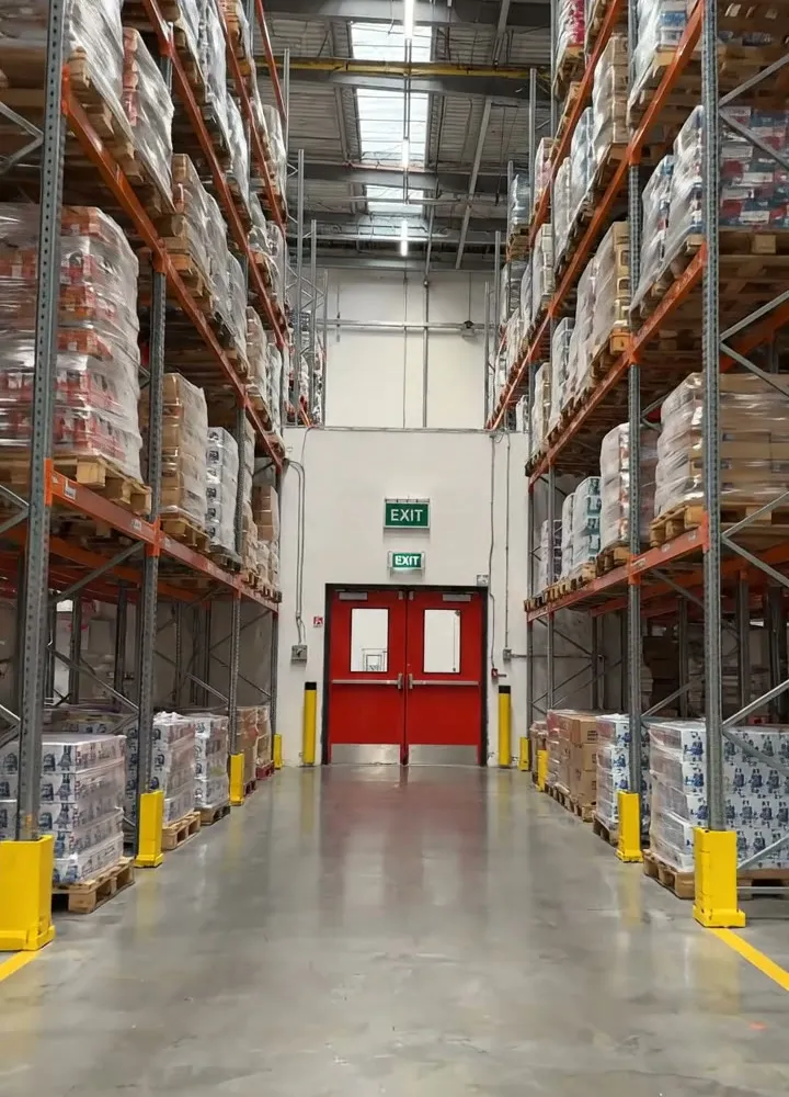 A warehouse aisle between tall pallet racks, with a red fire exit door at the far end