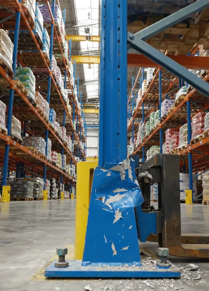 A blue racking upright dented and bent just above its base plate, with flakes of paint on the warehouse floor