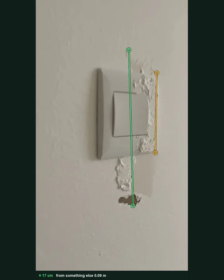 Plaster pulled away around a light switch, marked with a green measuring line against the switch plate as the reference, giving about 17 cm