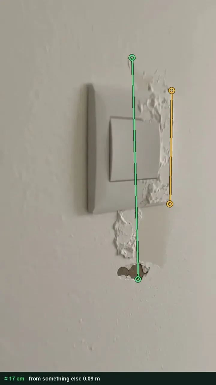 Light switch on a white wall with plaster pulled away above and below it, measured at 17 cm against the switch plate