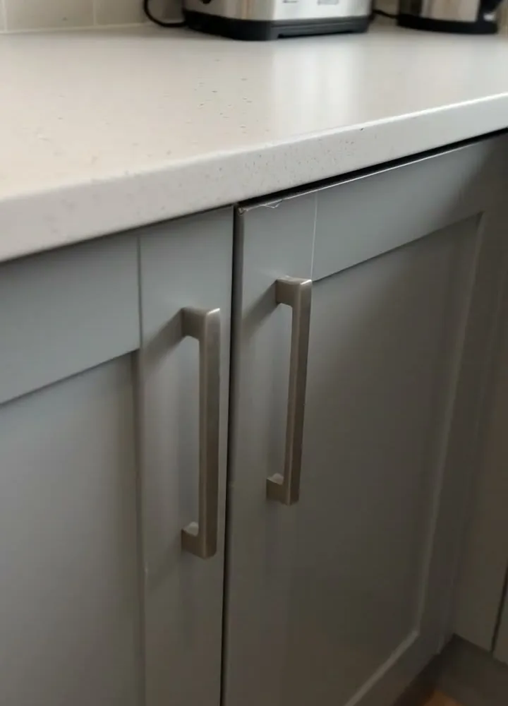 Grey shaker style kitchen base unit doors with long bar handles under a white worktop with a toaster