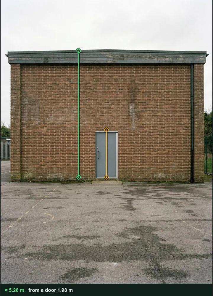 The brick end wall of a school sports hall marked up in Measure from photo: an amber line on the door and a green line from the ground to the fascia, about 5.26 m