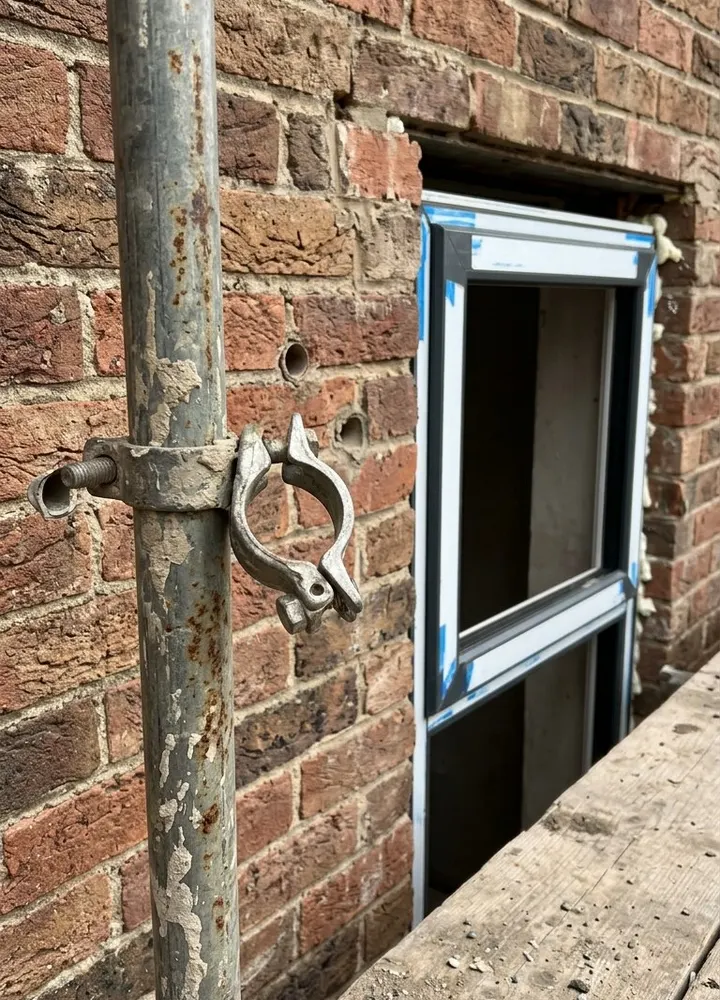 A scaffold standard beside a new window opening with a loose coupler where a tie has been removed