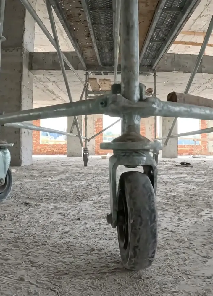 The castor of a mobile access tower on a dusty concrete floor