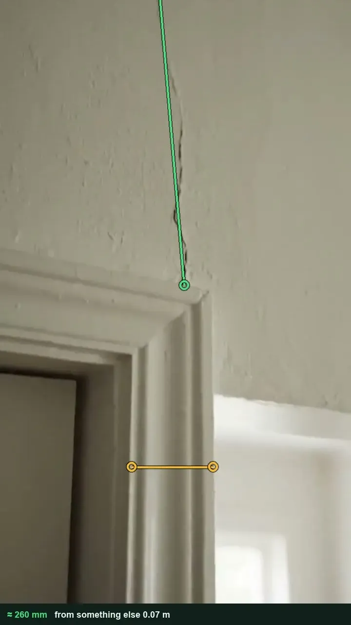 Painted plaster wall with a crack rising from the corner of a door architrave, marked with a green measuring line