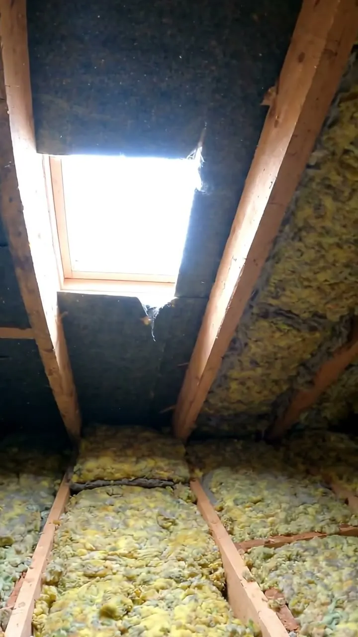 Roof space with torn roofing felt beside a chimney and daylight showing through the gap