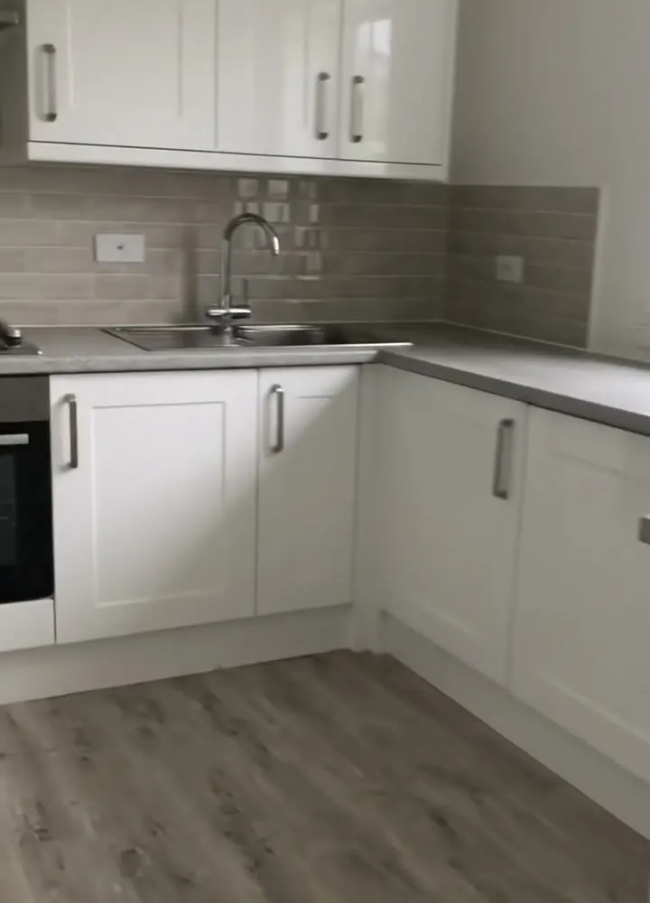 A new kitchen with white shaker units, a pale tiled splashback and a grey wood effect floor