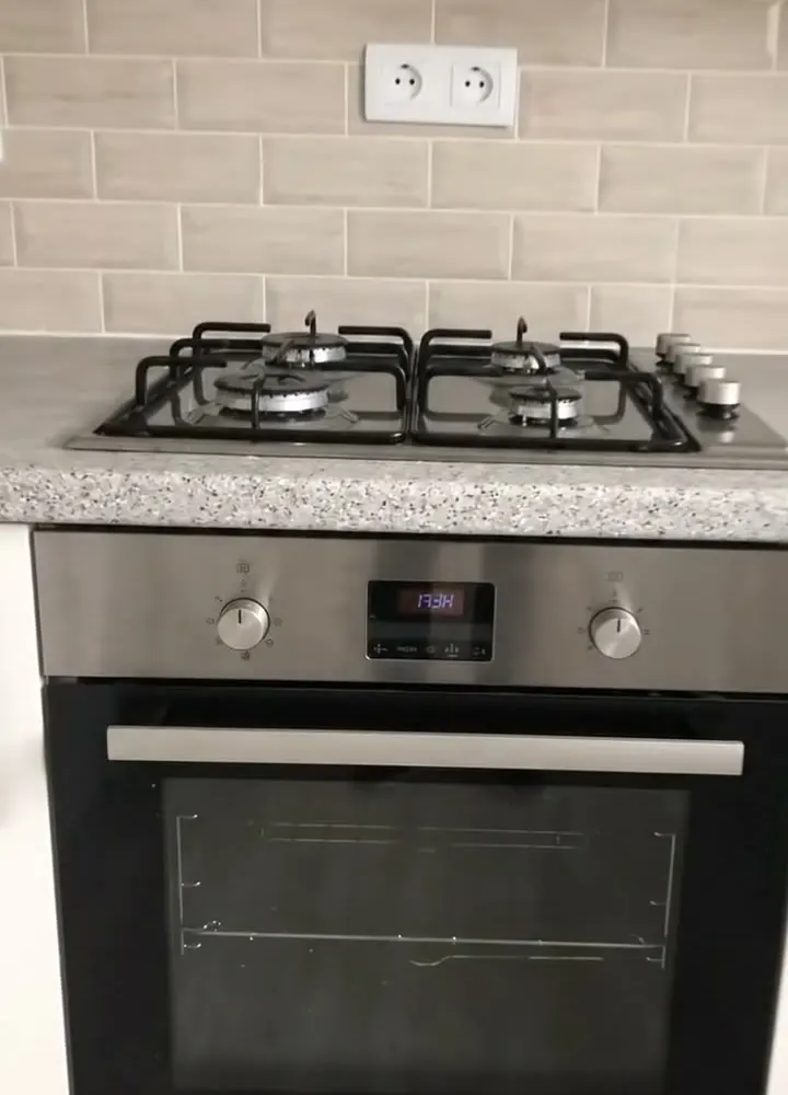 A built-in stainless steel oven under a four burner gas hob on a speckled worktop