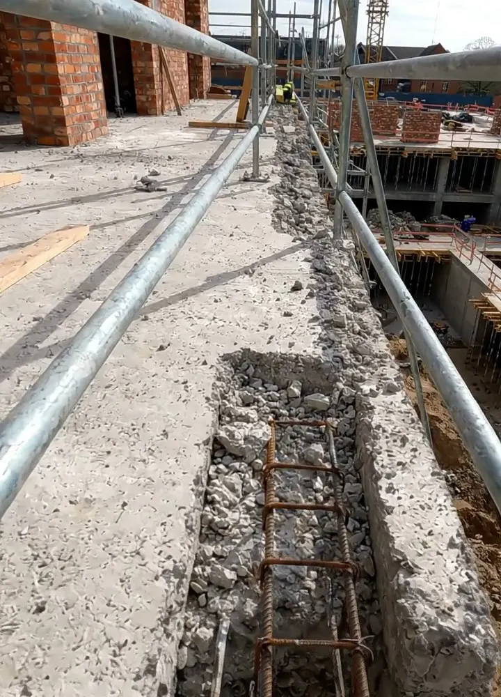 An open column pocket with exposed reinforcement on a slab edge beside scaffold tube guardrails