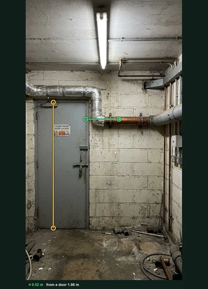 A plant room wall marked up in Measure from photo: an amber line on the door and a green line along a bare copper pipe, about 0.52 m