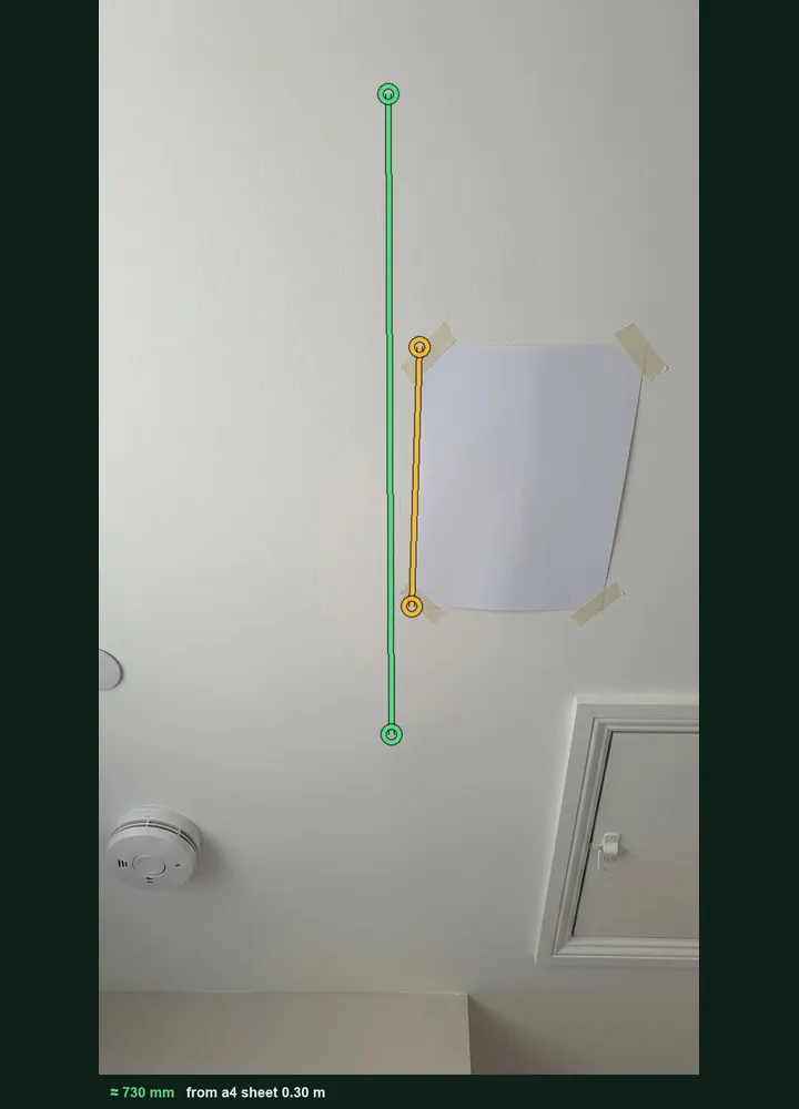 A landing ceiling with an A4 sheet taped beside a hairline crack, marked up in Measure from photo at about 730 mm