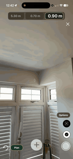 Aiming the phone at a corner in augmented reality — a dotted measuring line extends to the corner and the length appears as a chip along the top