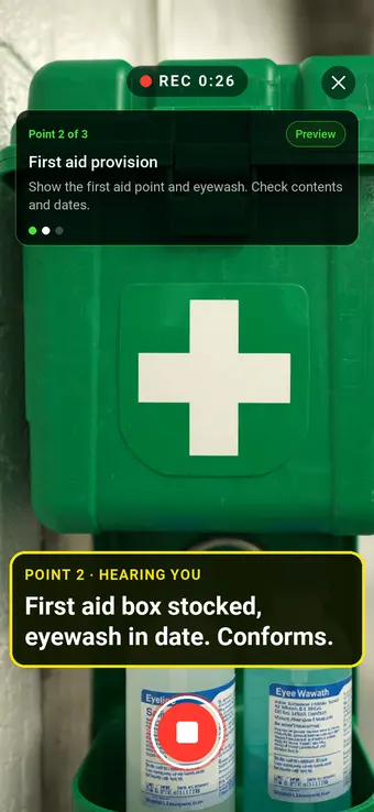 A wall-mounted first aid box and eyewash station, with the Walk Cam point card and live transcription