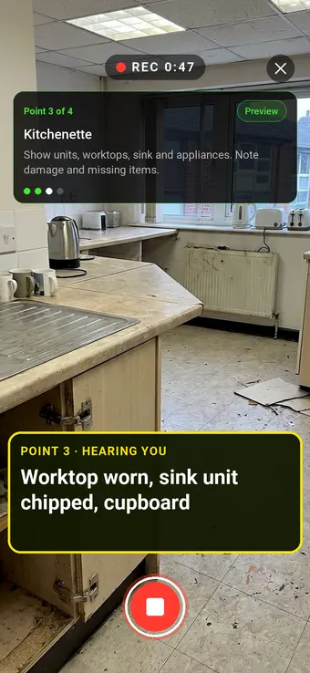 An empty office kitchenette with a worn worktop and missing cupboard doors, with the Walk Cam point card and live transcription