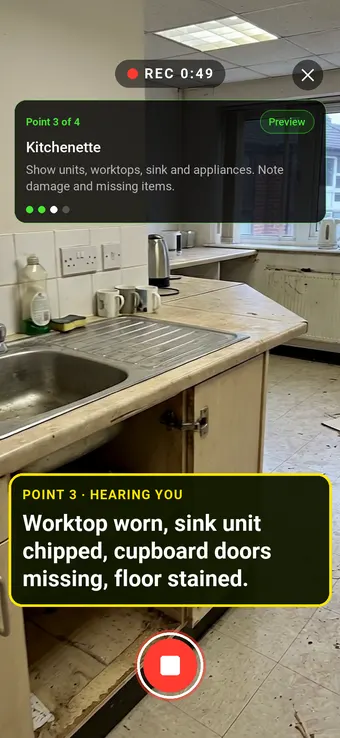 An empty office kitchenette with a worn worktop and missing cupboard doors, with the Walk Cam point card and live transcription