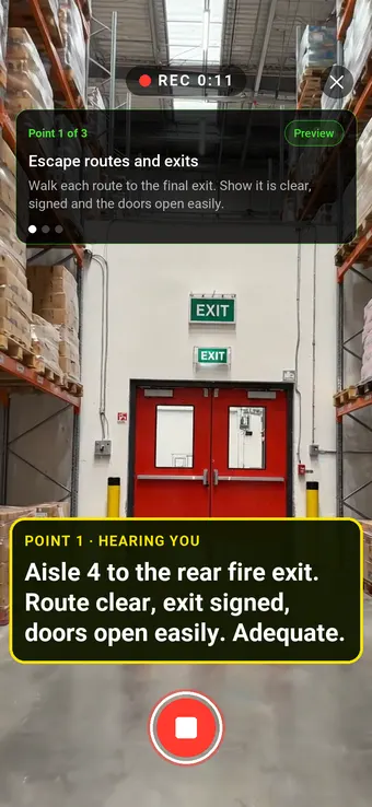 Walking a warehouse aisle to a signed double fire exit with SiteSurvey Walk Cam, while live voice-to-text writes the escape route finding into the assessment