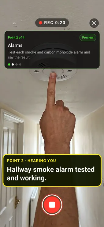A finger pressing the test button on a hallway smoke alarm, with the Walk Cam point card and live transcription