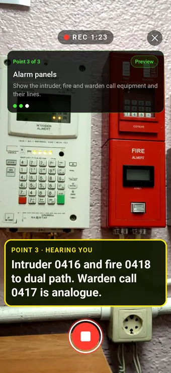 Intruder and fire alarm panels on an office wall filmed in Walk Cam, with the point card and live transcription